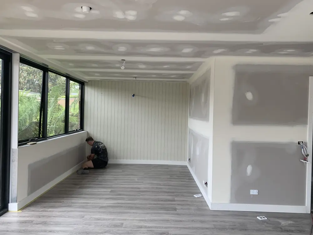 Painter working inside a partially prepared room with wall and ceiling surfaces in progress