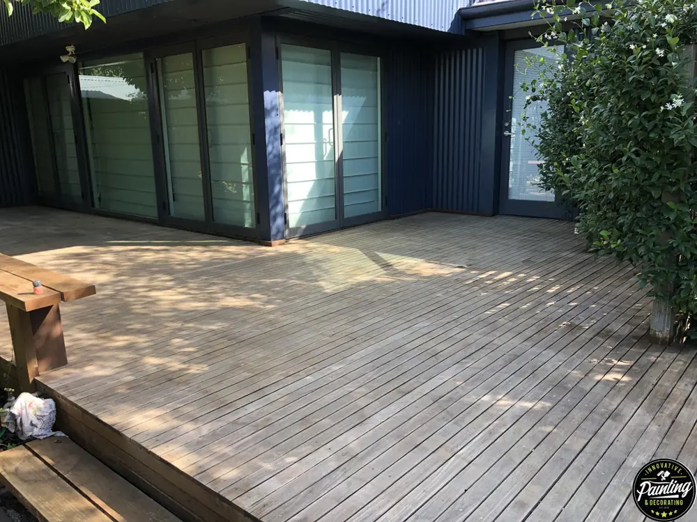 Large weathered timber deck before restoration beside a dark-clad home
