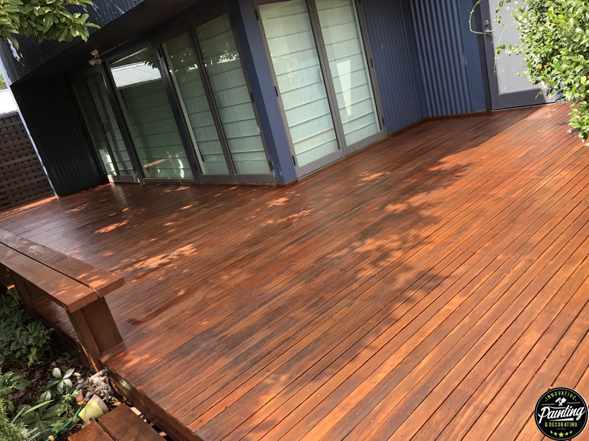 Freshly restored timber deck with a rich warm finish beside a dark-clad home