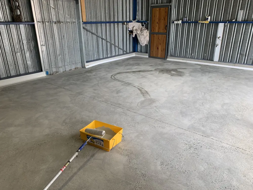 Concrete floor being prepared with a long-handled roller and work equipment
