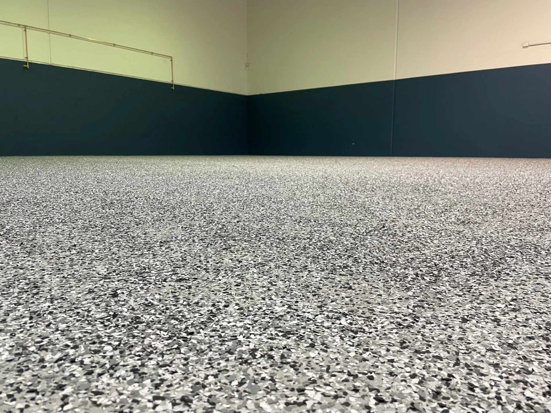 Finished speckled epoxy floor across a large workshop with dark lower walls