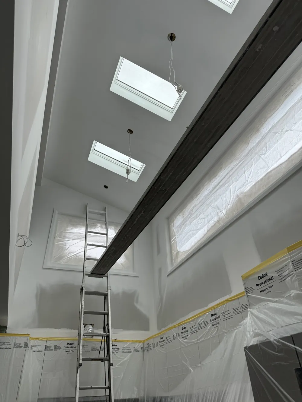 High interior wall and skylit ceiling being painted with a ladder in place