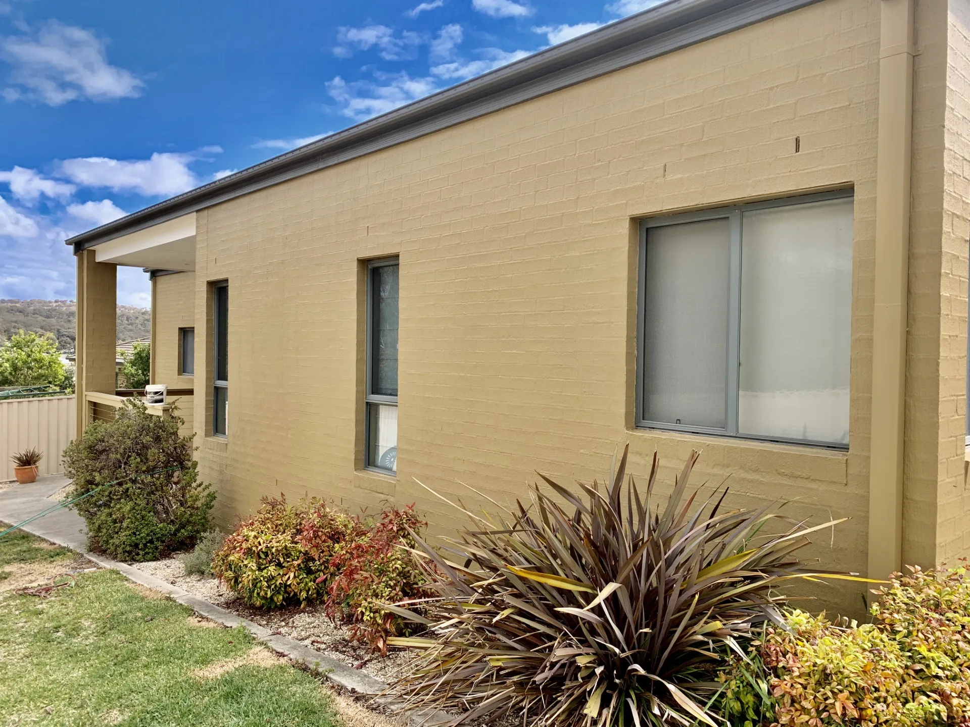 Freshly painted light-toned brick home exterior beside landscaped garden beds