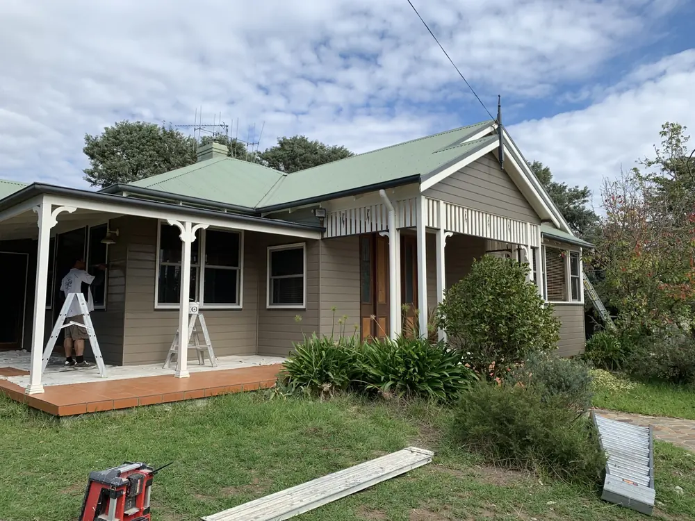 Heritage-style home exterior during restoration with a green metal roof and work equipment